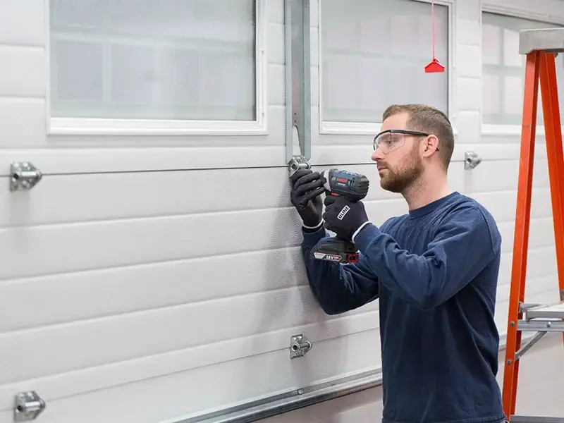 Technician installing garage door components with power drill, focused on alignment and repair, ensuring smooth operation and functionality.