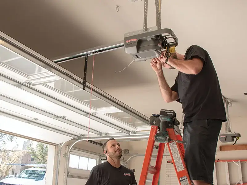 Technician installing a garage door opener while another technician observes, demonstrating expert garage door repair services.
