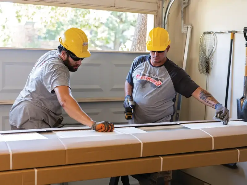 Two technicians in hard hats assembling a residential garage door in a garage, demonstrating installation services for Overhead Door Company of the Antelope Valley™.