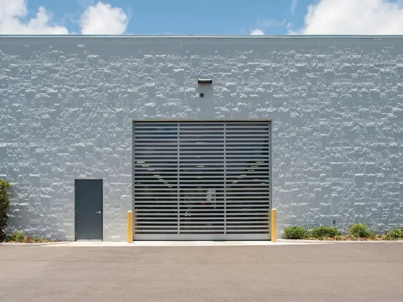 Commercial high-speed garage door with horizontal slats, installed in a gray industrial building, enhancing efficiency and accessibility for logistics and storage facilities.