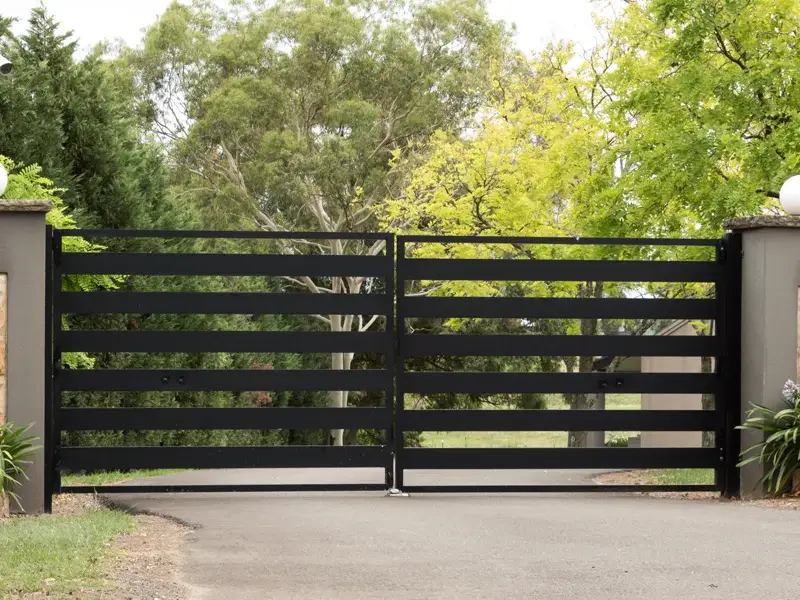 Black horizontal slat gate at a residential entrance, surrounded by greenery, illustrating secure access solutions for commercial and industrial properties.