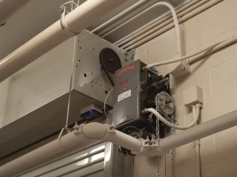 Commercial garage door operator system mounted on wall, featuring advanced motor technology and heavy-duty components for reliable performance in business environments.