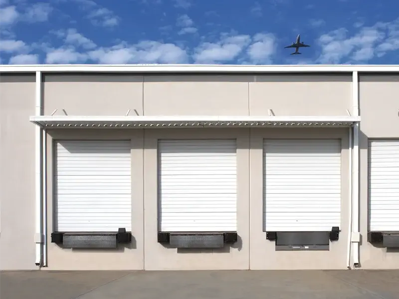 Commercial garage door loading docks with white roll-up doors and reinforced structures, designed for wind resistance and durability in industrial settings.