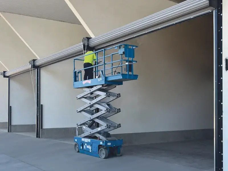 Technician using a scissor lift to perform maintenance on a commercial garage door, ensuring safety and efficiency for Overhead Door Company of the Antelope Valley™ services.