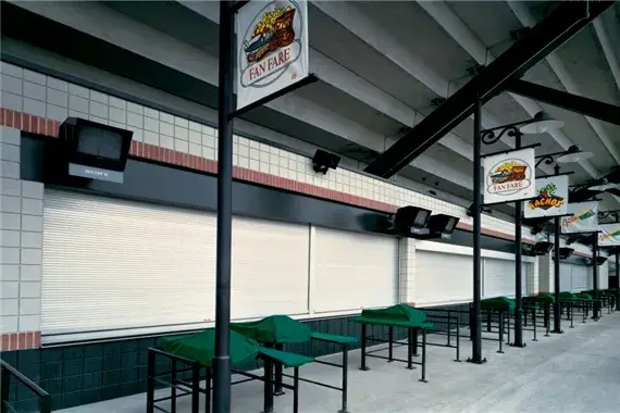 Rolling counter doors in a commercial setting with signage for food vendors, featuring closed metal shutters and empty serving areas.