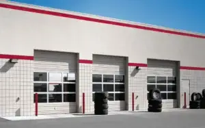 Commercial sectional steel garage doors with windows, featuring red trim, installed on a modern building exterior, showcasing reliable design for various business applications.