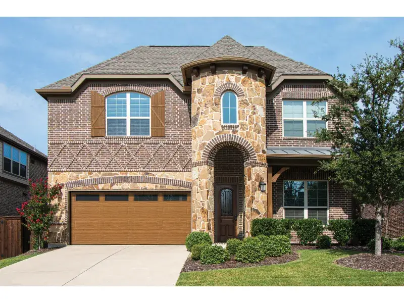 Traditional steel garage door enhancing curb appeal of a modern home with stone and brick facade, surrounded by landscaped greenery.