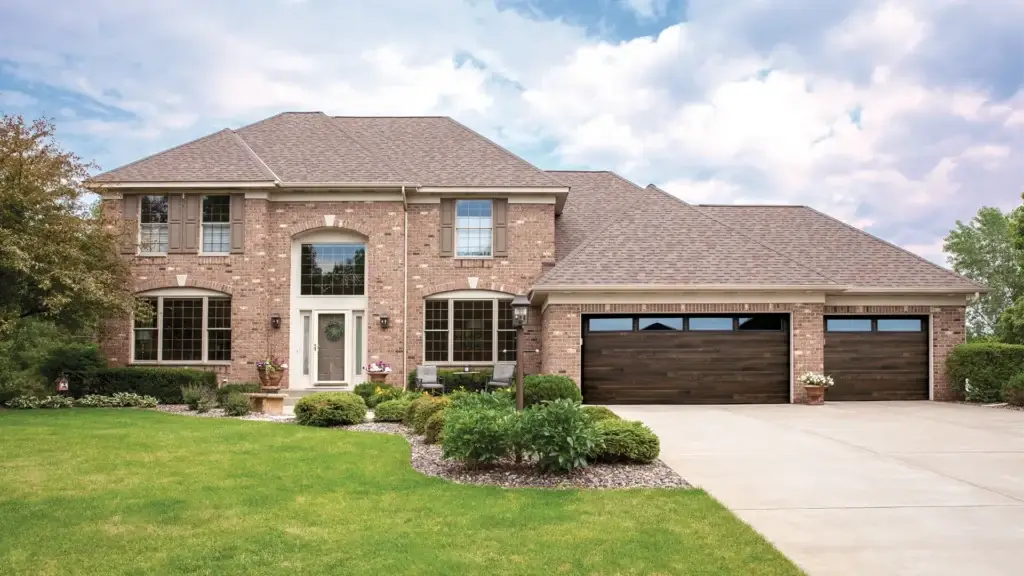 Residential home featuring brick exterior, lush front lawn, and modern garage doors enhancing curb appeal.